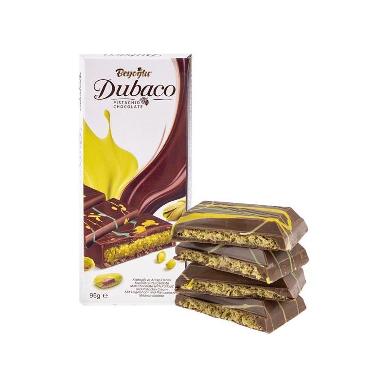 A box of Twice as Sweet Beyoglu Dubaco Dubai Pistachio Chocolate (Turkey) sits beside four stacked pieces, revealing pistachio layers and vibrant green-yellow decoration—a perfect treat for fans of Middle Eastern desserts.