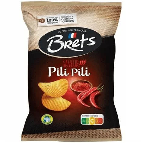 A 125g bag of Twice as Sweet Brets Pili Pili Chips from France is shown with black and tan packaging, ridged spicy chips, red chili peppers, French text, and nutritional scores—highlighting this bold snack.