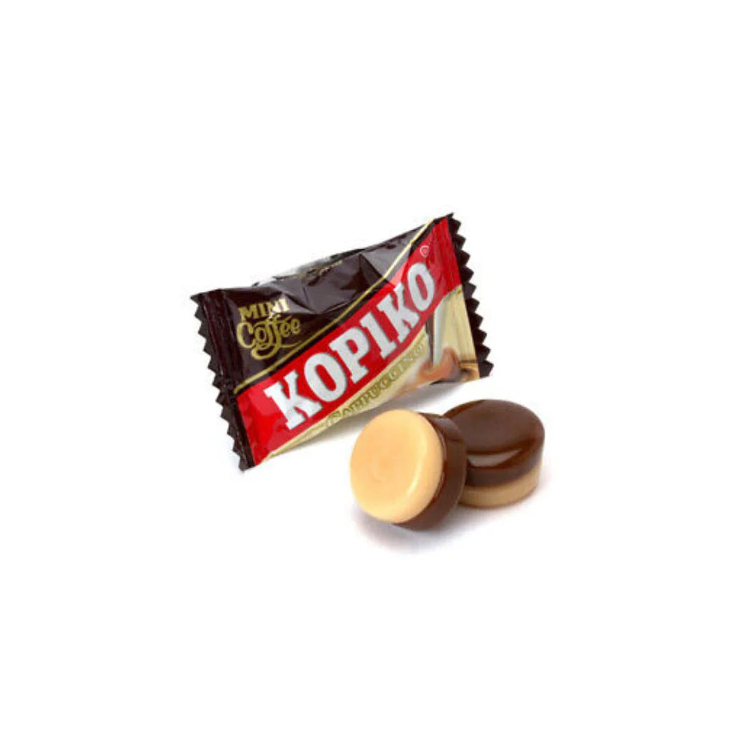 A Kopiko Cappuccino Candy 120g (Indonesia) by Twice as Sweet, in its brown and cream wrapper, with two unwrapped round candies beside it showing creamy light and dark cappuccino-inspired layers.