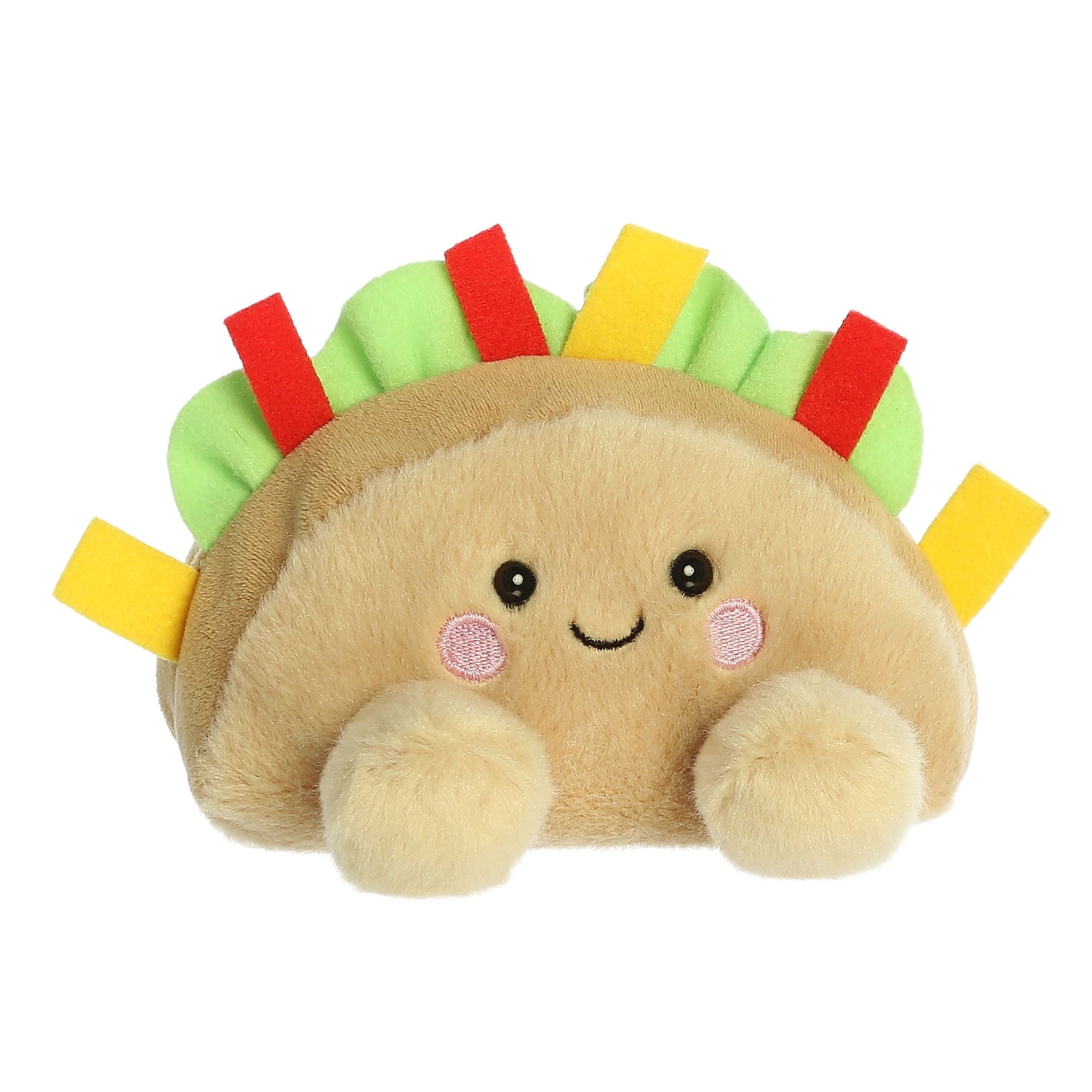 The Palm Pal Fiesta Taco by Twice as Sweet is a colorful plush toy with a smiling face, rosy cheeks, vibrant felt toppings, and two fluffy paws—perfect as a fun party companion.