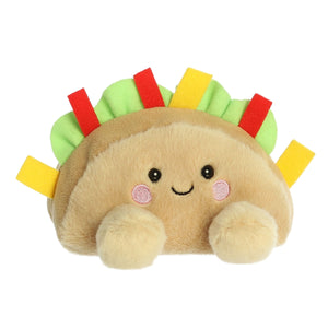 The Palm Pal Fiesta Taco by Twice as Sweet is a colorful plush toy with a smiling face, rosy cheeks, vibrant felt toppings, and two fluffy paws—perfect as a fun party companion.
