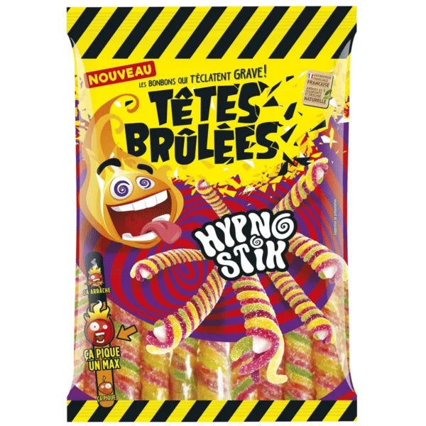 The Twice as Sweet Têtes Brûlées Hypnostik 180g pack from France features twisted, sugar-coated sour candy sticks on bright packaging with a cartoon character showing a zany expression and swirly eyes against vivid stripes.