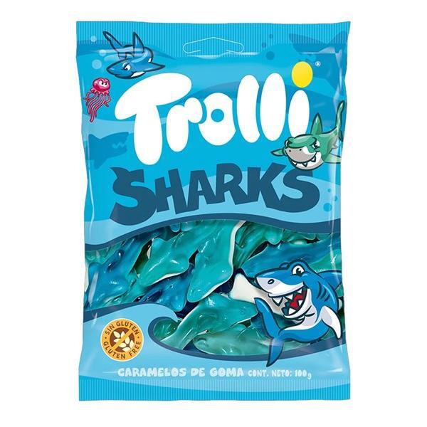 A blue and white bag of Twice as Sweet Trolli Sharks 100g (Spain) shows cartoon sharks and a jellyfish. The shark-shaped fruity gummies are gluten-free, with the package containing 100g of delicious Trolli Sharks candy.
